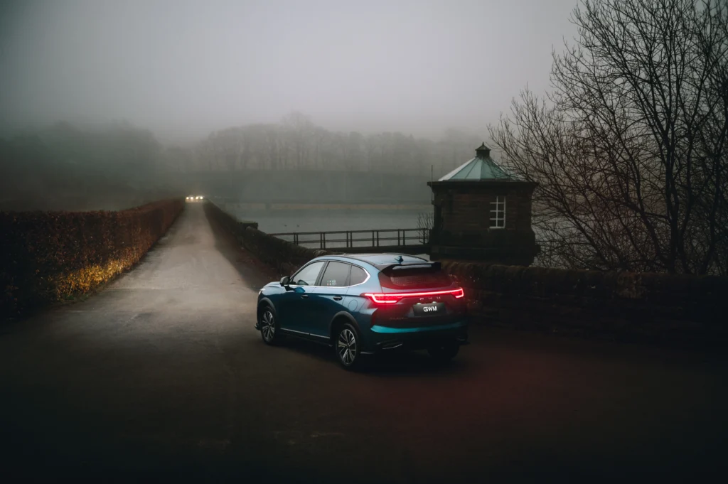 GWM Haval at dusk with lights on with two other vehicle headlights.