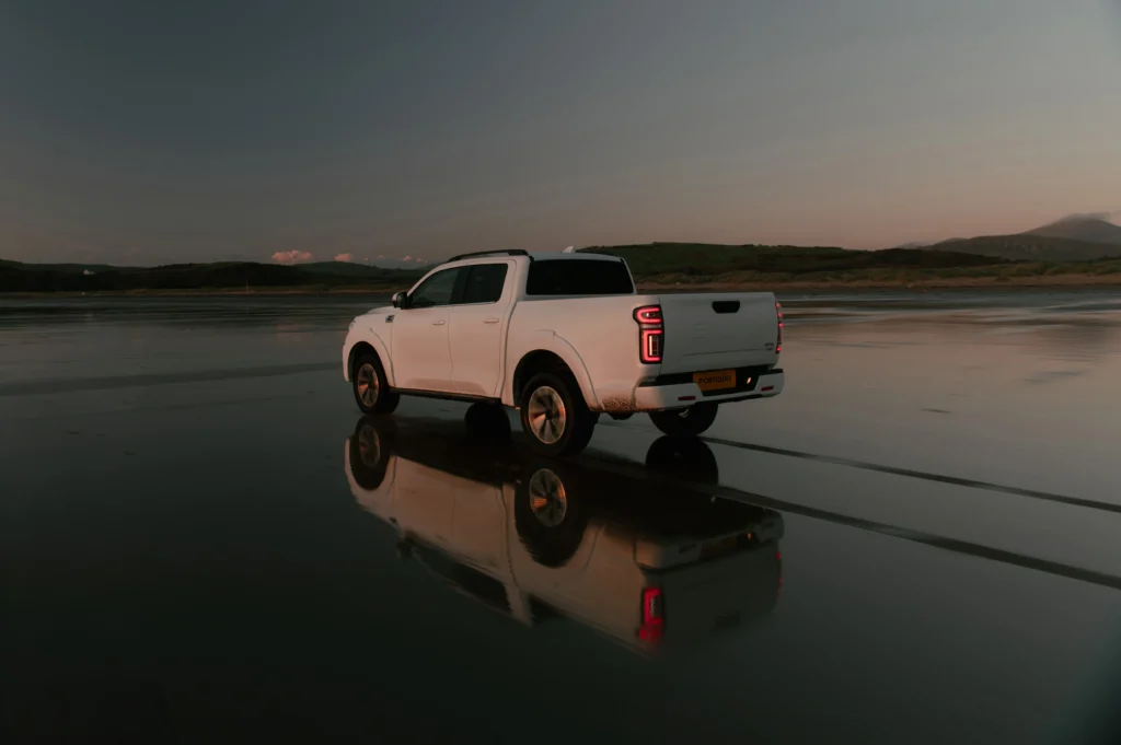 White GWM POER 300 driving along wet beach with reflection. 